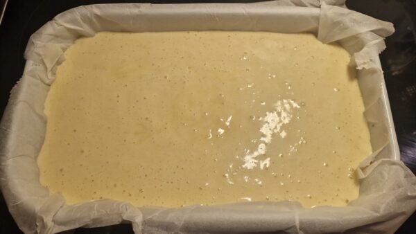 Kuchenteig in einer rechteckigen, mit Backpapier ausgelegten Form