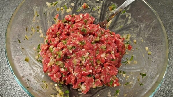Gewürfeltes Rindfleisch wird vorsichtig mit den Würzzutaten vermischt